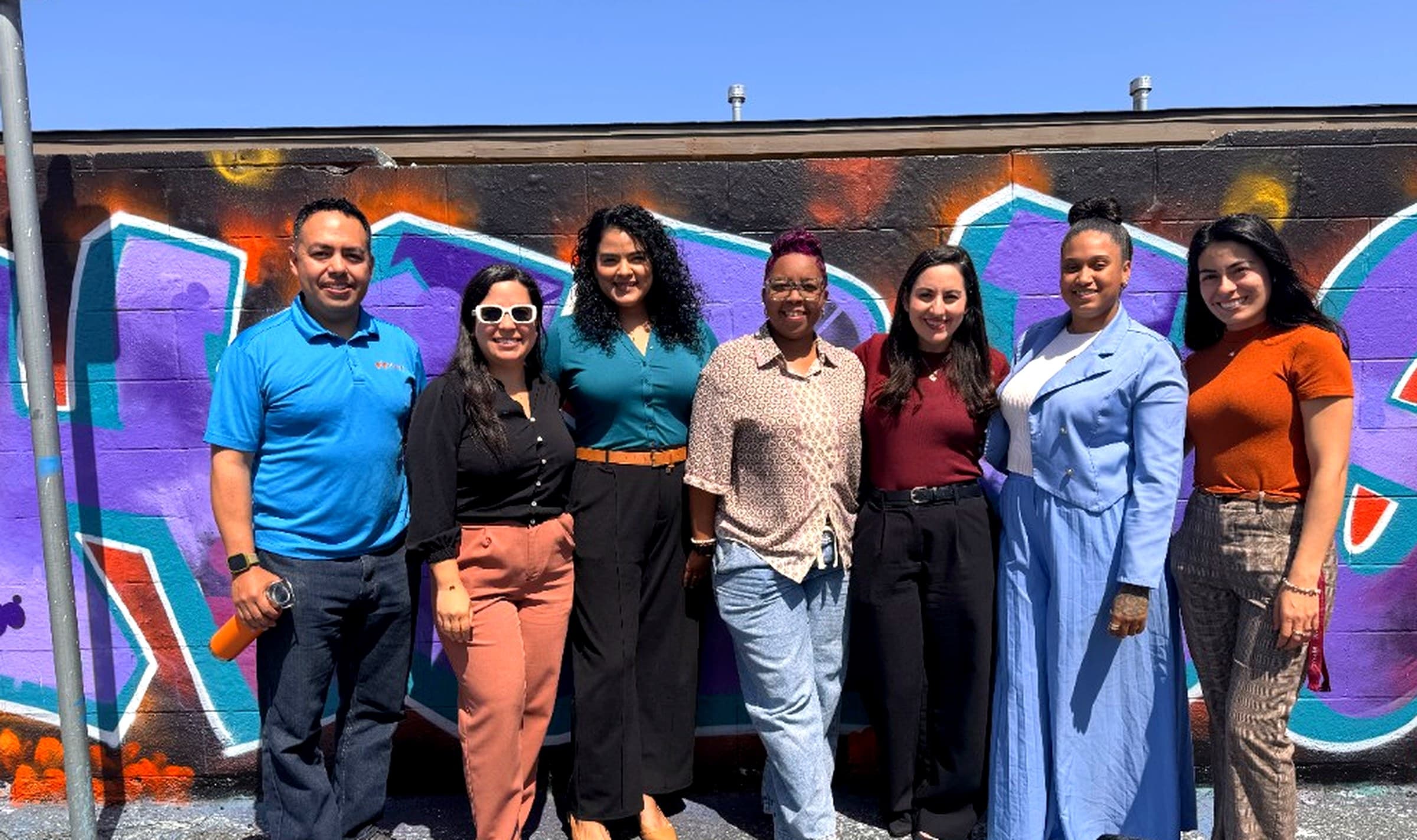 MAAC Family Asset Building team members smiling together in front of a colorful mural